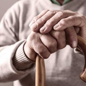Mani di un anziano che regge un bastone da passeggio. Paziente con tracheostomia.