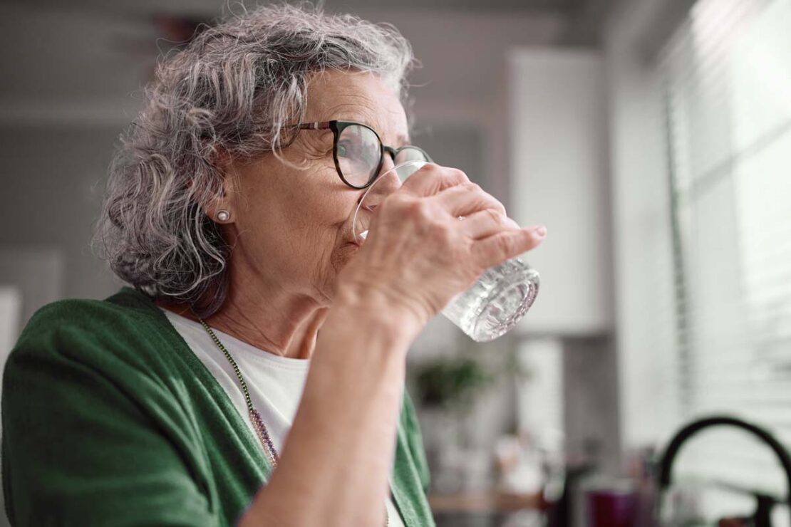 Una donna anziana beve un bicchiere d'acqua, per prevenire la disidratazione e il colpo di calore durante i mesi estivi.