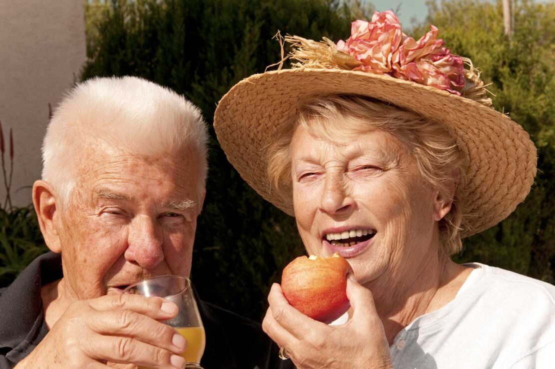 Coppia di anziani beve e mangia frutta. Mantenere gli anziani idratati e nutriti d'estate è cruciale contro il caldo.
