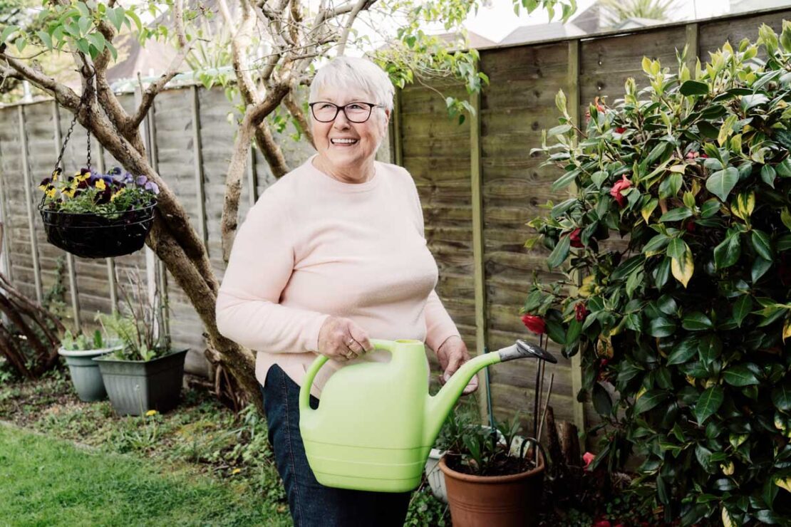 Donna anziana in giardino innaffia le piante. Gli anziani possono stare all'aperto, ma è bene evitare le ore più calde.